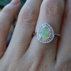 May include: A pear-shaped opal ring with a halo of smaller diamonds set in silver.