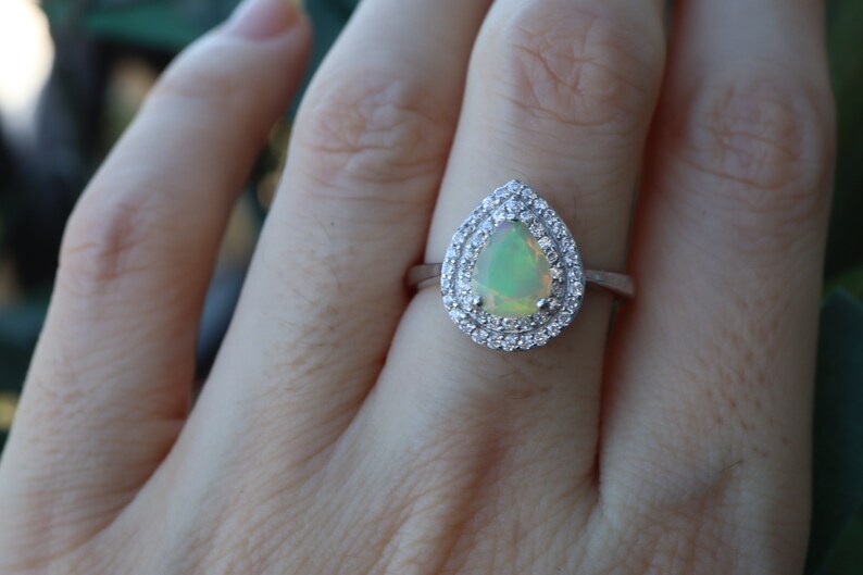 May include: A pear-shaped opal ring with a halo of smaller diamonds set in silver.