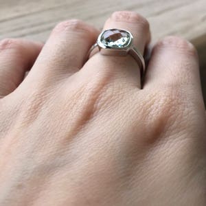 Puede incluir: Un anillo de plata con una piedra preciosa cuadrada de color verde claro.