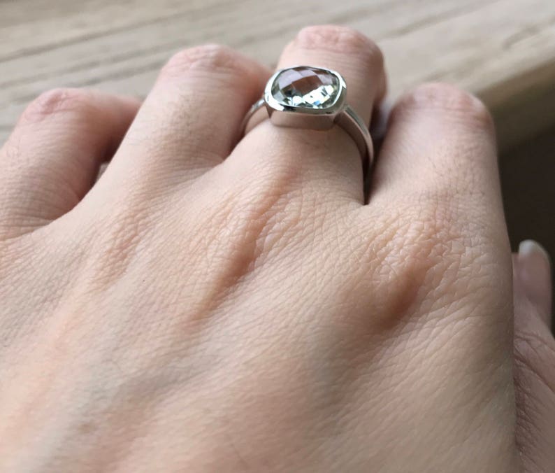 Puede incluir: Un anillo de plata con una piedra preciosa cuadrada de color verde claro.
