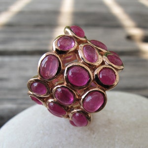 May include: A gold ring with a cluster of pink gemstones. The ring is set with multiple oval-shaped stones, creating a unique and eye-catching design.