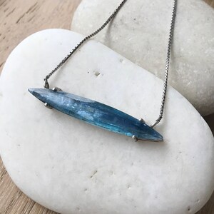 May include: A silver chain necklace with a long, pointed, blue-green gemstone pendant.