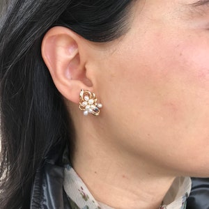 May include: A pair of gold tone earrings with a cluster of white pearls and black stones in a floral design.