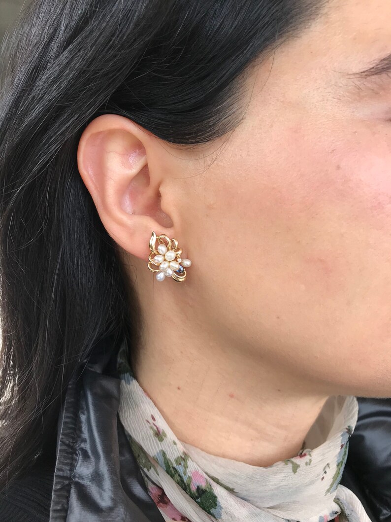 May include: A pair of gold tone earrings with a cluster of white pearls and black stones in a floral design.