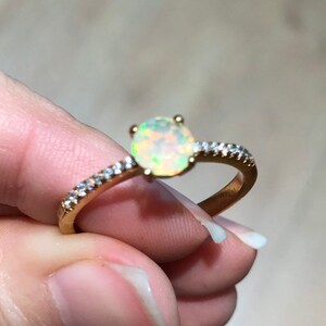 Pode incluir: Um anel de ouro com uma pedra de opala branca e uma banda de pequenos diamantes.
