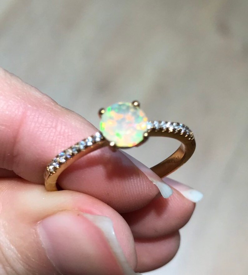 Pode incluir: Um anel de ouro com uma pedra de opala branca e uma banda de pequenos diamantes.