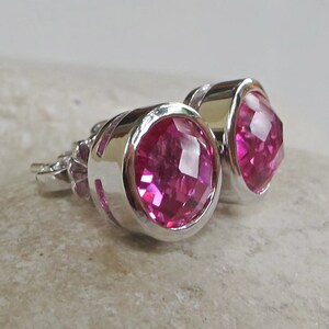 Puede incluir: Un par de pendientes de bot&oacute;n de plata con piedras preciosas facetadas de color rosa.