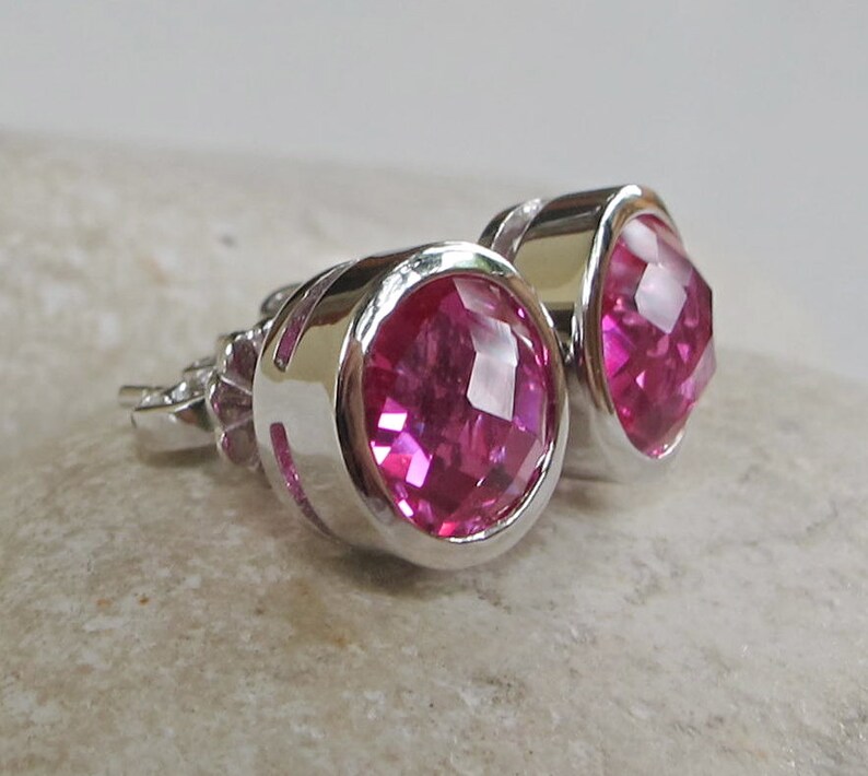 Puede incluir: Un par de pendientes de bot&oacute;n de plata con piedras preciosas facetadas de color rosa.