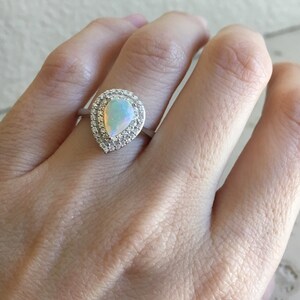 May include: A pear-shaped opal ring with a halo of small clear stones set in silver.