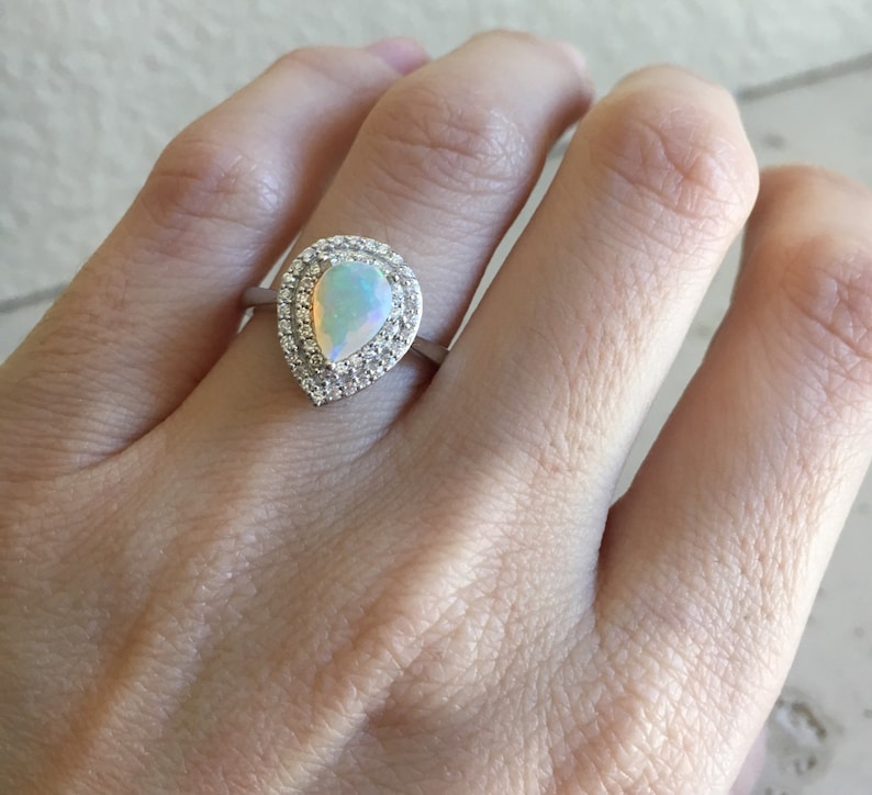 May include: A pear-shaped opal ring with a halo of small clear stones set in silver.