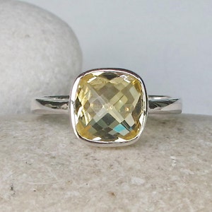 May include: A silver ring with a large, cushion-cut, yellow gemstone.