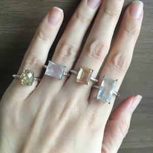 Peut inclure: Quatre bagues en argent avec des pierres précieuses de différentes couleurs. Les bagues présentent une pierre précieuse transparente de forme carrée, une pierre précieuse rectangulaire brun clair, une pierre précieuse rectangulaire transparente et une pierre précieuse ronde jaune.