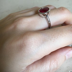 May include: A silver ring with a large, oval-shaped, red gemstone set in a bezel setting.
