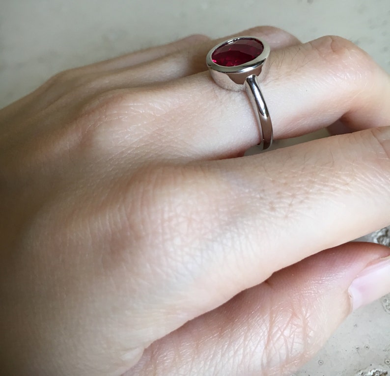 May include: A silver ring with a large, oval-shaped, red gemstone set in a bezel setting.