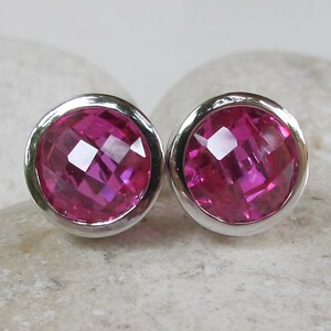 Puede incluir: Un par de pendientes de bot&oacute;n de plata con piedras preciosas facetadas de color rosa.