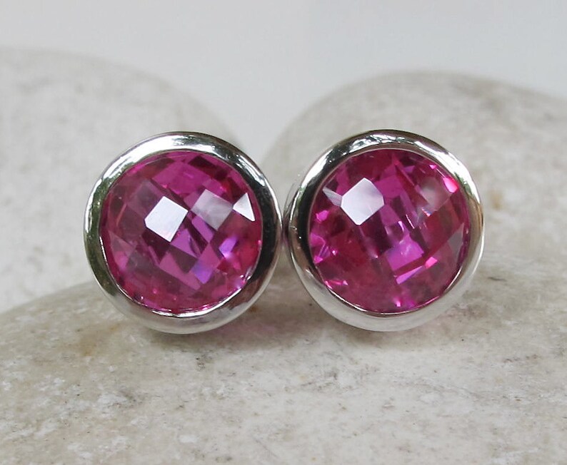 Puede incluir: Un par de pendientes de bot&oacute;n de plata con piedras preciosas facetadas de color rosa.