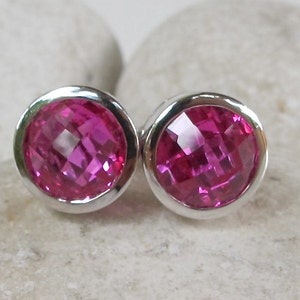 Puede incluir: Un par de pendientes de bot&oacute;n de plata con piedras preciosas facetadas de color rosa.