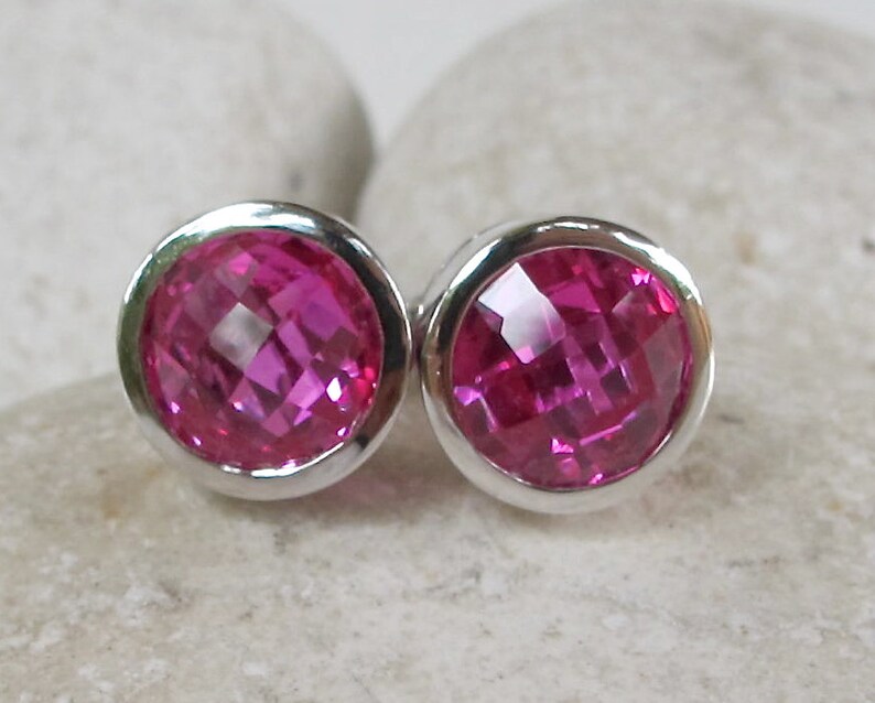 Puede incluir: Un par de pendientes de bot&oacute;n de plata con piedras preciosas facetadas de color rosa.