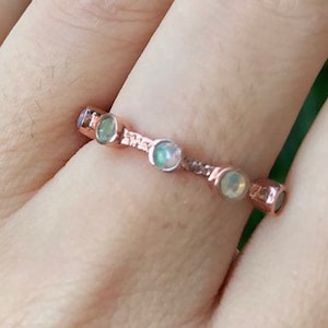 May include: A rose gold ring with five small, round, iridescent opal stones set in a delicate band.