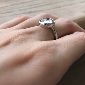 Puede incluir: Un anillo de plata con una gran piedra preciosa de talla coj&iacute;n transparente.