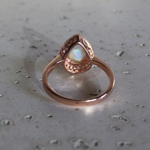 May include: A rose gold ring with a pear-shaped opal gemstone set in a halo of smaller stones.