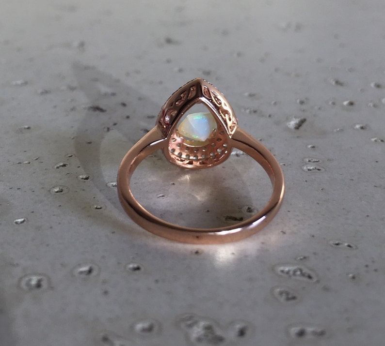 May include: A rose gold ring with a pear-shaped opal gemstone set in a halo of smaller stones.