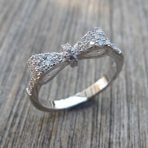 Puede incluir: Un anillo de plata con un diseño de lazo adornado con piedras de circonita cúbica transparentes.