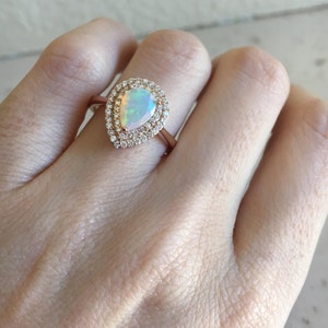 May include: A pear-shaped opal ring with a double halo of small diamonds set in rose gold.