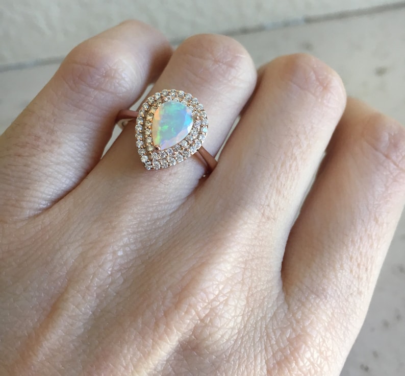 May include: A pear-shaped opal ring with a double halo of small diamonds set in rose gold.