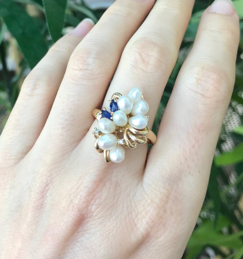 May include: A gold ring with a cluster of white pearls and blue gemstones. The ring is set on a gold band.