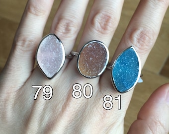 May include: Three rings with silver bands and colourful, textured stone settings. The stones are in shades of pink, brown, and blue. Each ring has a different shape, with the numbers 79, 80, and 81 visible.