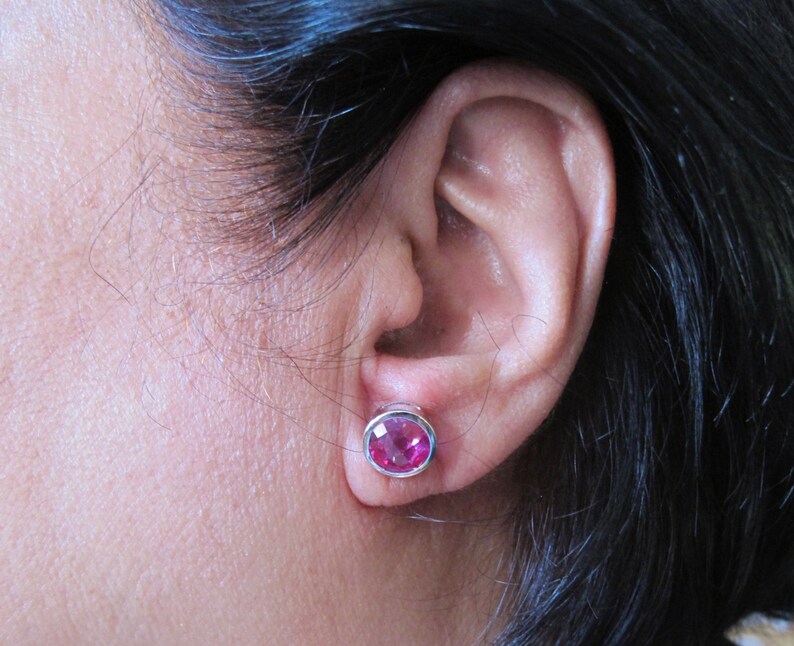 Puede incluir: Primer plano de la oreja de una persona con un pendiente de piedra preciosa rosa. El pendiente est&aacute; engastado en plata y tiene forma redonda.