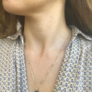 Op de afbeelding: Een gouden ketting met een groene edelsteen hanger. De hanger is druppelvormig en heeft een gouden ontwerp rond de rand. De ketting wordt ook gedragen met bijpassende groene edelsteen oorbellen.