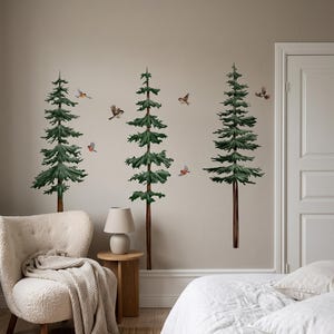 May include: A set of wall decals featuring three tall, green pine trees with brown trunks and several small, colorful birds in flight. The trees are depicted in a detailed, illustrative style, arranged vertically on a plain, neutral-colored wall.