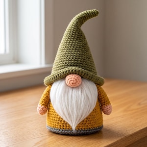 Può includere: Una statuetta di gnomo all'uncinetto con un cappello alto e appuntito verde oliva, un corpo giallo senape e una lunga barba in pelliccia sintetica bianca. Lo gnomo ha un piccolo naso rotondo color pesca e mani abbinate, con un bordo grigio.