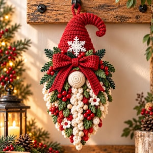 May include: A crocheted gnome wall hanging featuring a tall red hat with a white snowflake, a large red bow, and a long white beard decorated with green leaves, red berries, and small white flowers. The gnome is suspended from a wooden board.