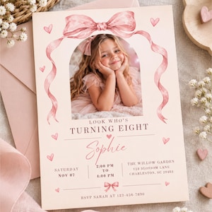 May include: A rectangular birthday invitation card in pale pink featuring a watercolor illustration of a large pink bow framing a central photo of a child. The text reads: Look who's turning eight, Sophie, Saturday Nov 07, 2:00 PM to 4:00 PM, The Willow Garden, 123 Blossom Lane, Charleston, SC 29403, RSVP Sarah at 123-456-7890.