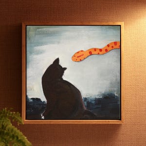 May include: A square framed painting featuring a silhouette of a black cat sitting and looking towards an orange snake with red spots. The background is a textured light blue and white sky above a dark blue ground, all encased in a wooden frame.