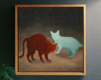 May include: A square framed painting featuring two cats on a dark brown surface against a black background. One cat is a solid deep red color, while the other cat is a pale light blue. The frame is made of light-colored wood with a simple profile.