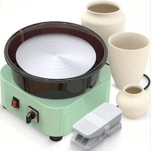 May include: A mint green electric pottery wheel with a circular silver turntable, a black splash guard, and a grey foot pedal. Three unglazed, off-white ceramic vessels of varying sizes are positioned next to the machine, which features a red power switch and a black speed control knob.
