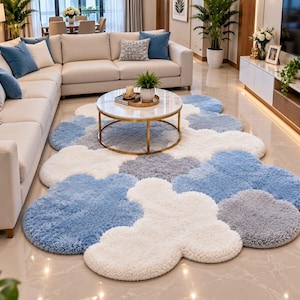 May include: A plush area rug featuring a cloud-shaped design in shades of white, light blue, and gray. The rug has a thick, textured pile and an irregular, organic outline that mimics the appearance of fluffy clouds layered across the floor.