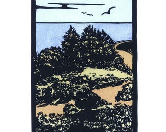 May include: A block print art piece titled Big Sur, featuring a coastal landscape with dark trees, a tan path, and a light blue ocean under a pale sky. Three birds are visible in the sky. The artist's initials DY and signature are present.