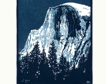 May include: A blue and white linocut print titled Half Dome at Twilight, depicting a mountain peak rising above a forest of pine trees. The artwork features a dark blue sky, a white mountain face with blue shadows, and a signature with 1/25.