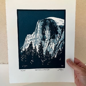 May include: A blue and white linocut print of Half Dome in Yosemite National Park at twilight. The print is signed and numbered 25/25.