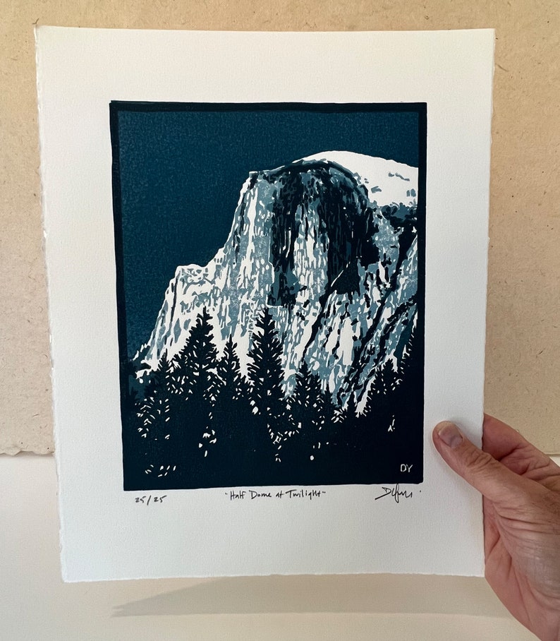 May include: A blue and white linocut print of Half Dome in Yosemite National Park at twilight. The print is signed and numbered 25/25.