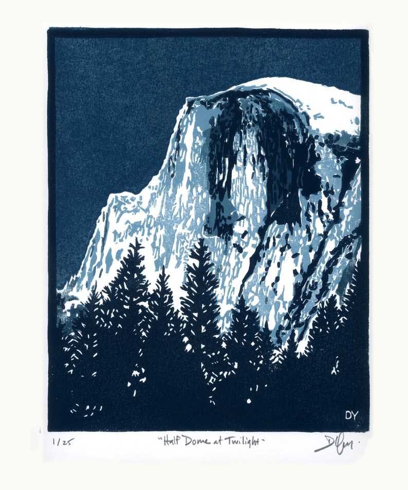 May include: A blue and white linocut print of Half Dome in Yosemite National Park at twilight. The print features a dark blue background with a white snow-capped mountain peak. The text "Half Dome at Twilight" is printed below the image.
