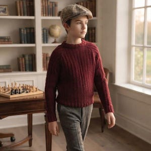 Peut inclure: Un pull en tricot à manches longues bordeaux avec une texture côtelée, porté avec un pantalon gris et une casquette plate à carreaux beige et marron. Le pull présente une encolure ronde et des manches longues, le pantalon est droit.