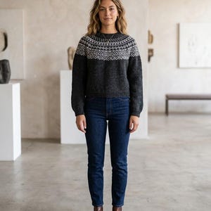 Può includere: Un maglione a maniche lunghe grigio antracite con un motivo geometrico bianco in stile Fair Isle attorno allo sprone e allo scollo, abbinato a jeans blu scuro e stivaletti in pelle marrone. Il maglione presenta girocollo, polsini e orlo a coste.