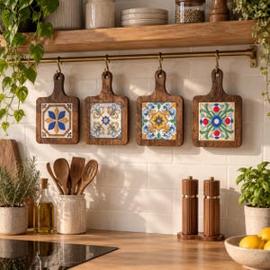 May include: Four square wooden cutting boards with decorative ceramic tiles in the center, hanging from a brass rail. Each board features a unique colorful floral pattern in blue, yellow, green, and red. The boards are displayed above a kitchen counter.