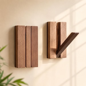 Op de afbeelding: Twee rechthoekige wandhaken van bruin hout. Elke haak bestaat uit drie verticale houten latten, waarbij één lat aan de rechterkant van de tweede haak naar buiten is gericht om te dienen als ophangpunt voor kleding of accessoires.